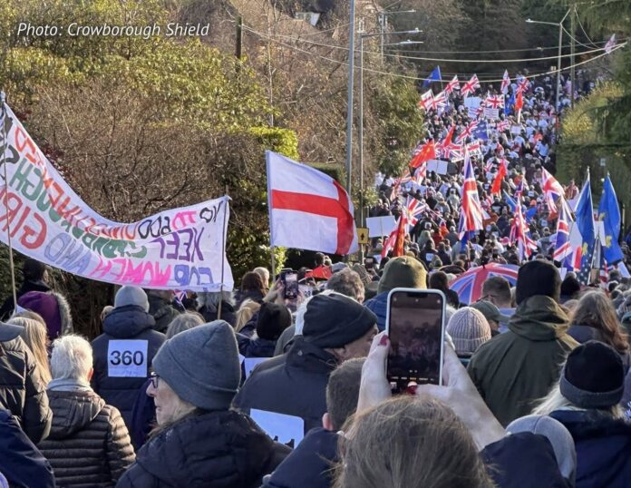 Large protest crowds march towards Crowborough carrying flags and placards